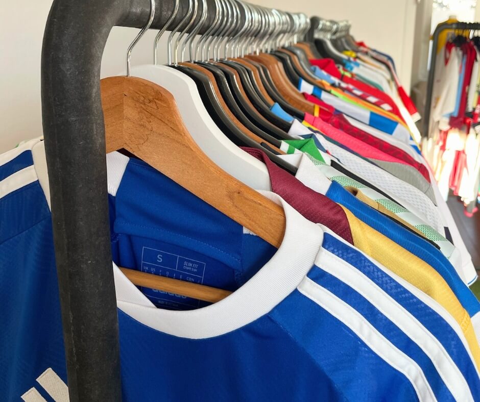 Rangée de maillots de sport multicolores suspendus sur des cintres, illustrant la diversité des équipes et des préférences des fans.