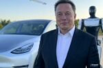 Elon Musk devant une Tesla blanche et le robot Optimus, illustrant la réunion Tesla T1 2025 sur l'avenir de la conduite autonome et de l'IA.