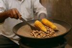 Un vendeur indien prépare du maïs et des cacahuètes grillés dans du sable chaud, illustrant une méthode de cuisson traditionnelle sans huile, utilisée depuis des siècles en Inde pour une cuisson naturelle et écologique.